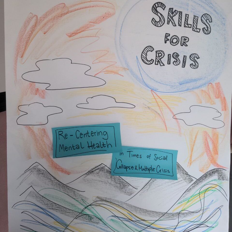 On white sheet of paper with colourful pencils the mountains, the clouds and the sky are drawn. There is also a logo of the project - Skills for Crisis drawn at the top right corner. There are two blue paper notes attached in the middle: one saying re-centering mental health, another - in times of social collapse and multiple crises